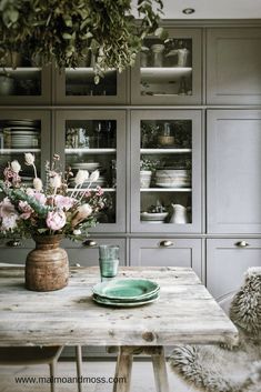 a wooden table topped with a vase filled with flowers next to a green plate on top of a wooden table