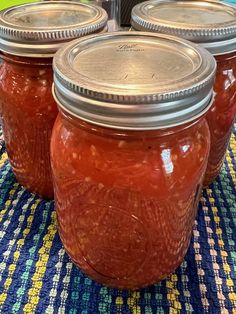 four jars filled with red liquid sitting on top of a blue and yellow table cloth