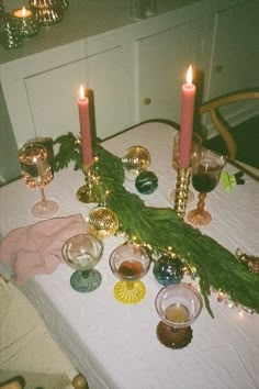 a table topped with candles and dishes covered in christmas greenery on top of a white table cloth