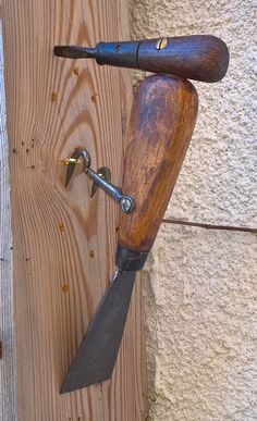 a wooden handle with two knives attached to it on a wood board wall next to a door