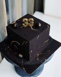 a three tiered black cake with gold numbers on it