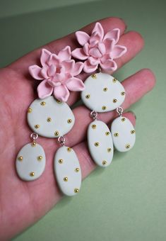 a hand is holding some white and pink earrings with flowers on it's sides