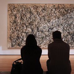 two people sitting in front of a large painting