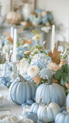 a table with blue pumpkins and white flowers on it, candlesticks in the background