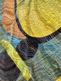 a close up view of an abstract quilt with wavy lines and curves in yellow, green, blue, orange and black