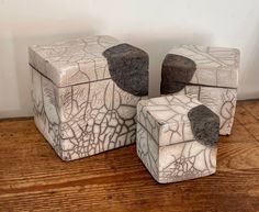 three white and black ceramic boxes sitting on top of a wooden table next to a wall