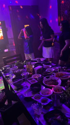 people standing around a table full of food and drinks in front of a tv screen