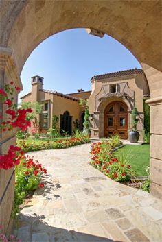 an archway leading to a house with red flowers in the foreground