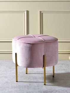 a pink velvet ottoman with gold legs in front of a white wall and beige walls