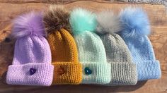 four knit beanies with pom - poms are lined up on a wooden surface