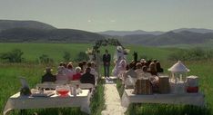 a group of people sitting at tables in the middle of a field with mountains behind them