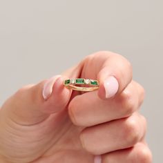 a woman's hand holding a gold ring with three emeralds on the band