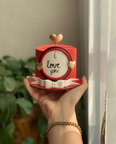 a hand holding a small red cake with i love you written on the top and heart decorations