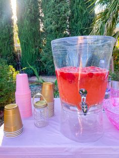 a pink drink is being poured into a clear pitcher on a table with gold cups