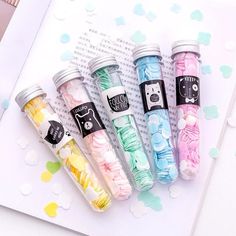 four small bottles filled with different colored confetti next to an open book on a table