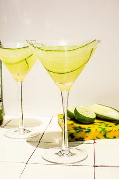 two martini glasses with cucumber and lemon on the side