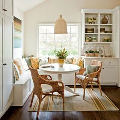 a kitchen with white walls and wooden flooring next to a dining room table surrounded by wicker chairs