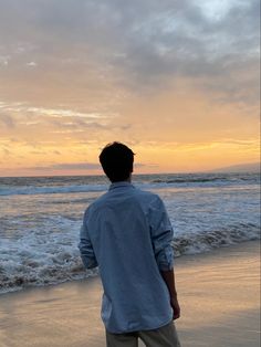 a man standing on top of a sandy beach next to the ocean at sunset or dawn