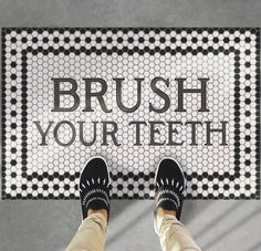 a person standing in front of a black and white bathroom rug that says brush your teeth