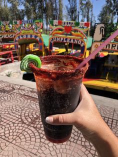 a person holding up a drink in front of carnival rides