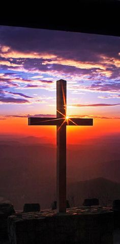 a cross on top of a hill with the sun setting in the distance behind it