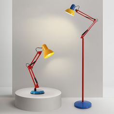 two red and yellow desk lamps sitting on top of a white table next to each other