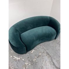 a large green curved couch sitting on top of a cement floor next to a white wall