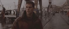 a man standing in front of a boat on a rainy day with other people walking around