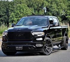 a black ram truck is driving down the road in front of some trees and bushes