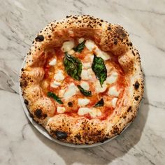 a pizza sitting on top of a white plate covered in cheese and spinach leaves