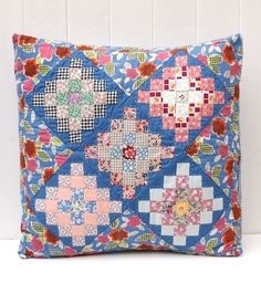 a blue pillow with colorful patchwork and flowers on the front, sitting against a white brick wall