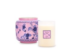 a candle next to a pink and blue container with flowers on it, both side by side