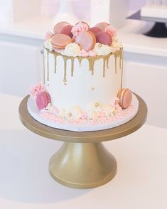 a white and gold cake with macaroons on top is sitting on a table