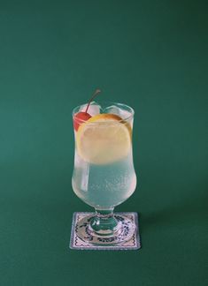 a glass filled with liquid sitting on top of a green table next to a slice of fruit