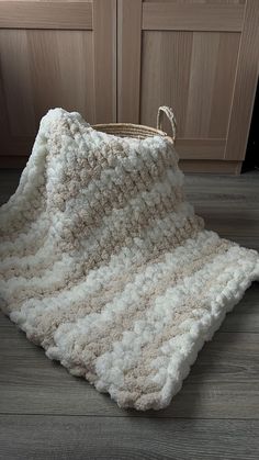 a crocheted blanket sitting on the floor next to a basket with handles in front of wooden doors