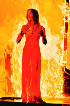 a woman standing in front of a fire with her hands on her chest and arms outstretched