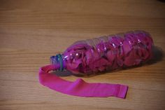 a plastic water bottle with pink fabric around it on a wooden table next to a rubber band