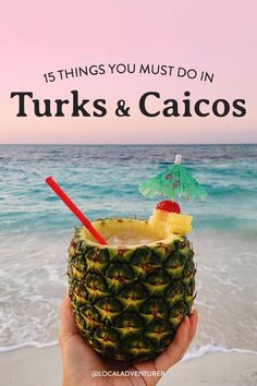 a person holding up a pineapple drink in front of the ocean with text that reads, 15 things you must do in turks & caecos