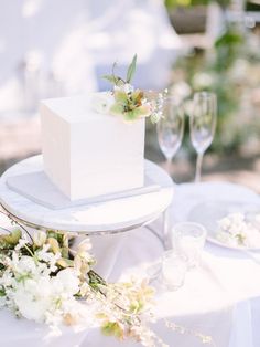 a white cake sitting on top of a table next to two wine glasses and flowers