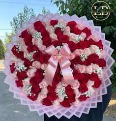 a person holding a large bouquet of red and white roses with pink ribbons on it