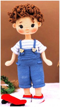 a crocheted doll wearing overalls and red shoes