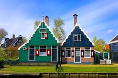 two green houses with red shutters next to a body of water in front of them