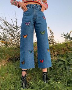 a woman standing in the grass with her hands on her hips and wearing butterfly patches