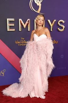 a woman in a pink feathered dress on the red carpet at an awards event