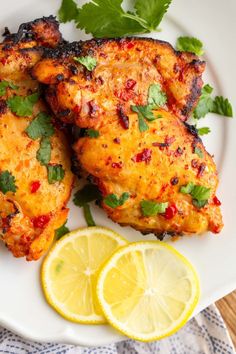 two pieces of chicken on a plate with lemons and cilantro