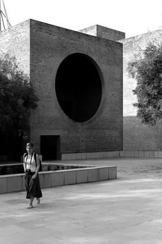 a woman standing in front of a building with a large round hole on it's side