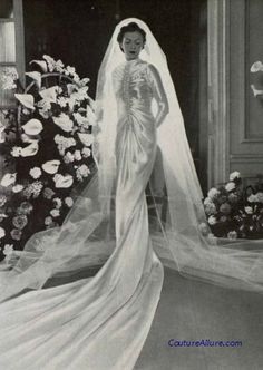 an old black and white photo of a woman in a wedding dress with flowers behind her