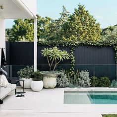 an outdoor living area with a swimming pool and potted plants on the side of the house