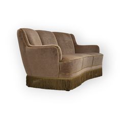 a brown couch with fringe trim on the armrests and back end, sitting in front of a white background