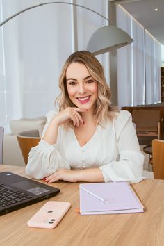 a woman sitting at a table in front of a laptop computer with a notepad on it